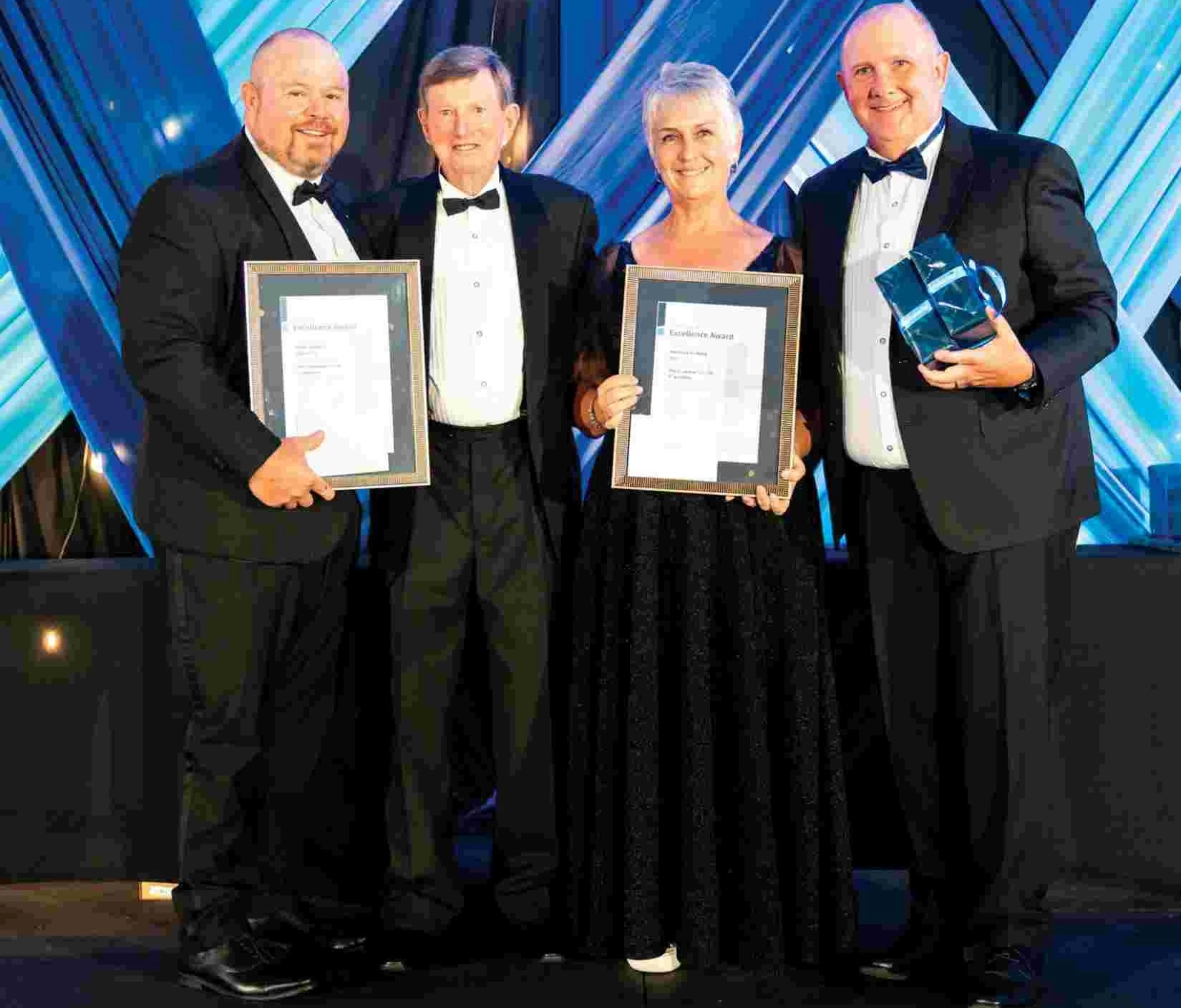 Four people in formal attire holding awards on stage